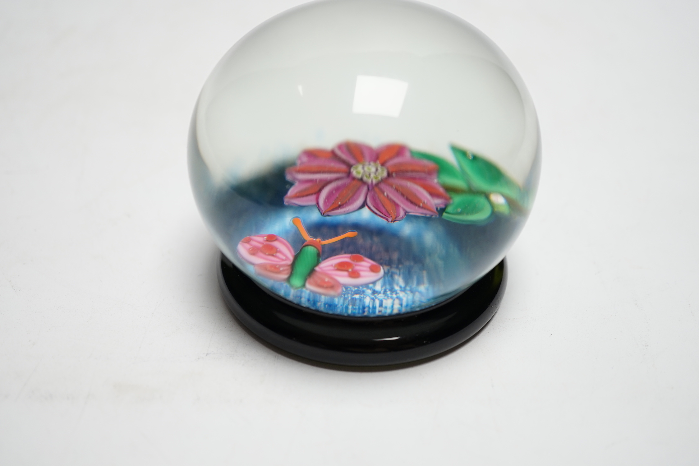 A rare Paul Ysart ‘insect and flower’ footed glass paperweight, Caithness period, scratched signature ‘P. Ysart’, ‘PY’ cane, decorated with a butterfly and pink dahlia, blue jasper ground, raised on a dark green glass fo